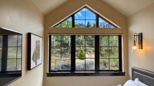 A high architectural triangle gable window left completely uncovered above standard bedroom windows to reveal mountains and a bright blue sky — BCC of Denver Colorado.; Transform your space with allergen-reducing treatments through Blind Corners & Curves serving Aurora, Steamboat Springs, and Grand Lake.; 