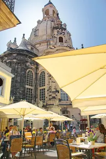 Außenterrasse im Ehrenhof des Coselpalais Dresden: Gäste unter großen Sonnenschirmen, im Hintergrund die Kuppel und Fassade der Frauenkirche.
