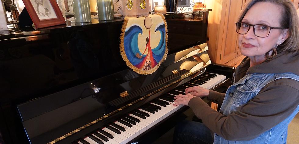 A woman with glasses plays a black piano, adorned with a colorful cloth featuring an artistic design, in a cozy room with wooden decor.