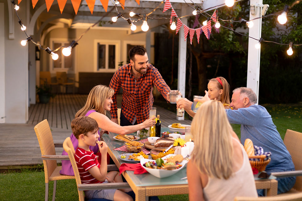 Family toasts at a festive outdoor dinner. Warm lighting and orange bunting create a cozy atmosphere. Smiles and laughter abound.