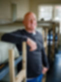 Tall man with shaved head and blondes stubble in a blue, long-sleeved shirt standing in front of a row of bunk beds. This man is Alan Evans. The picture is next to his welcome letter so people can learn about him and the nonprofit homeless shelter, Helping Hands.