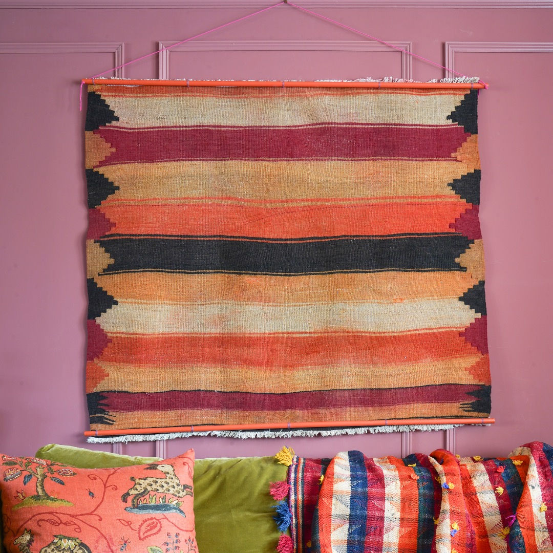 Orange, black & ivory wide striped woven vintage wall hanging tapestry hung on dark pink living room wall above green sofa