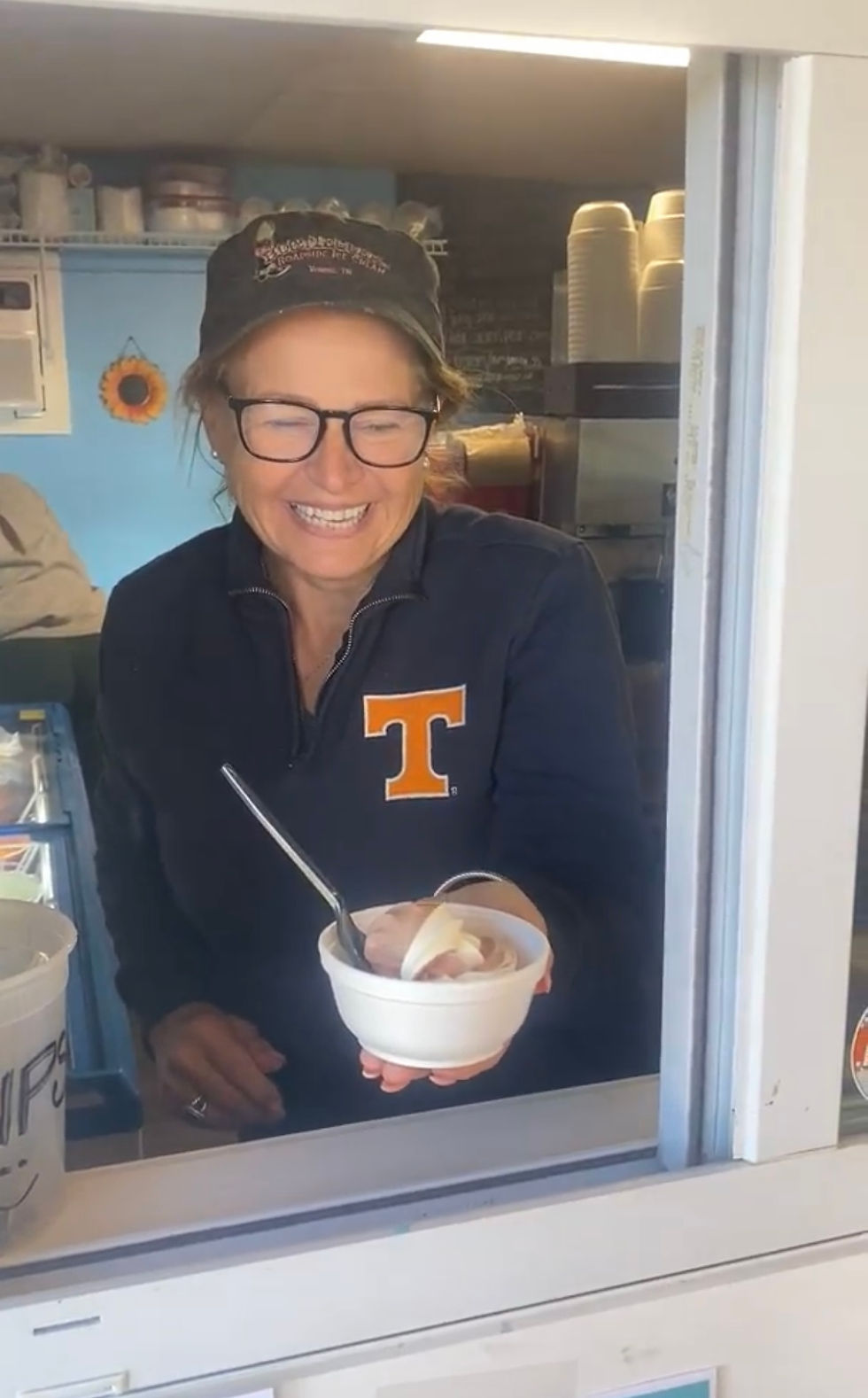 A smiling woman hands a cup of ice cream to the photographer