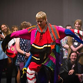 A young performer in brightly colured-costum surrounded by standing audience members