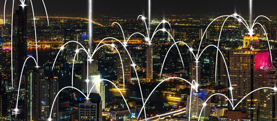 A vibrant city skyline at night with tall, illuminated buildings and glowing roads. White digital arcs connect various skyscrapers, representing seamless communication across the city. These arcs visually symbolize cloud phone service technology enhancing business connectivity through cloud-based telecommunication networks.