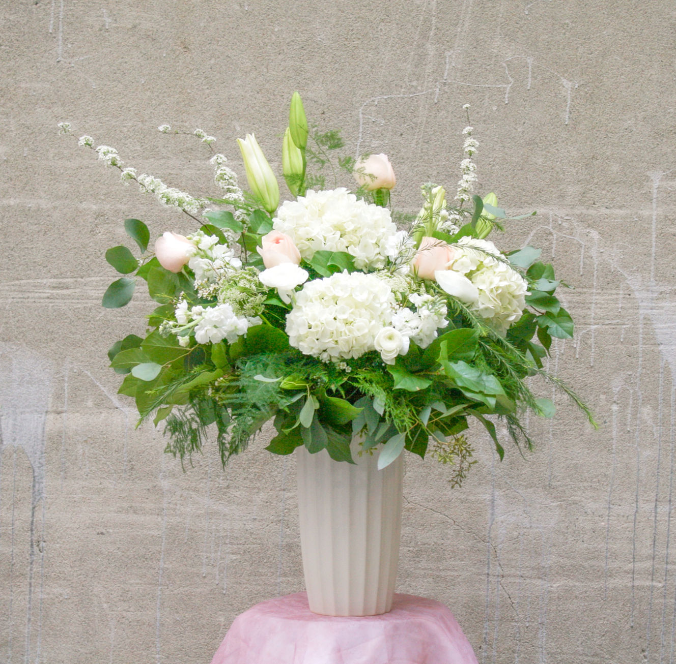 Tall floral arrangement of white hydrangeas pink garden roses designed with while lilies in a tall white vase