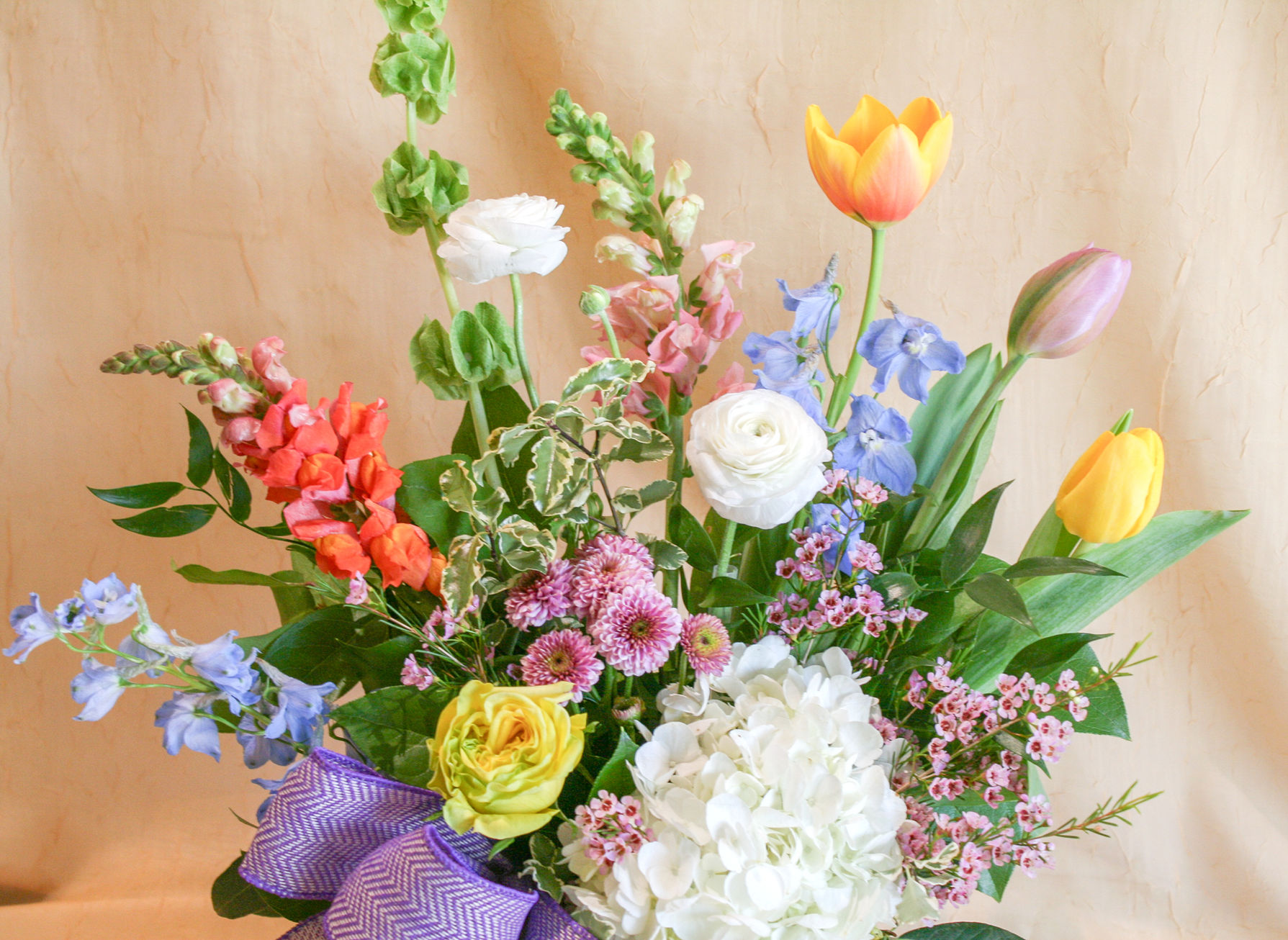 a stunning blend of hydrangea, roses, mums, tulips, snapdragons, bells of Ireland, and delphinium artfully arranged within a