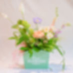 A fresh floral design featuring two products: a peace lily plant & a small vase of flowers nestled inside a decorative tin.