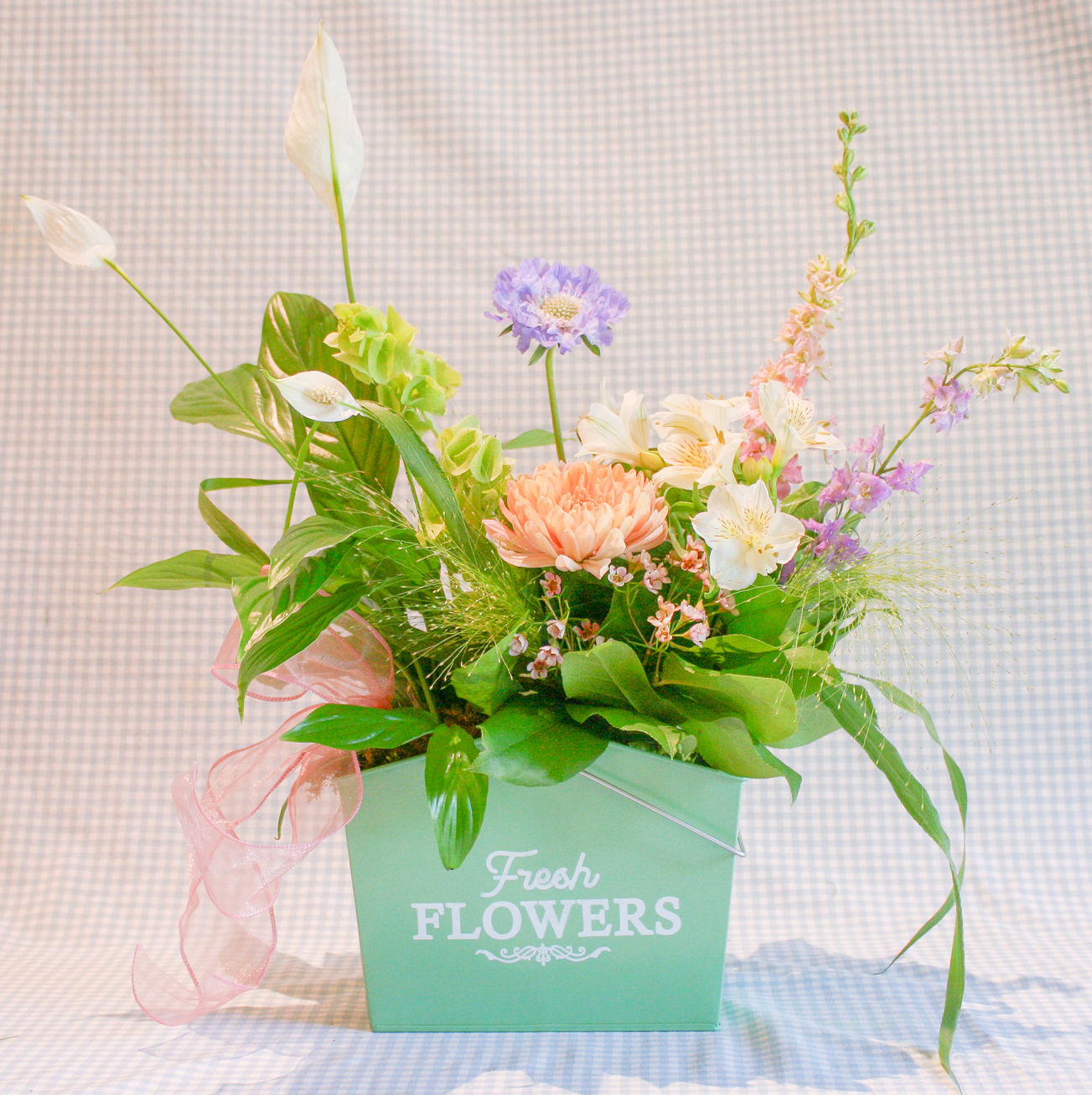A fresh floral design featuring two products: a peace lily plant & a small vase of flowers nestled inside a decorative tin.