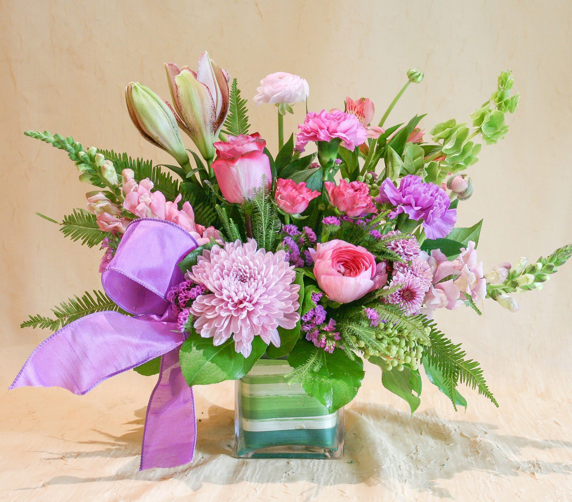 A fresh floral design arranged with pink & purple spring blooms like roses, ranunculus, chrysanthemum, snapdragons in a vase