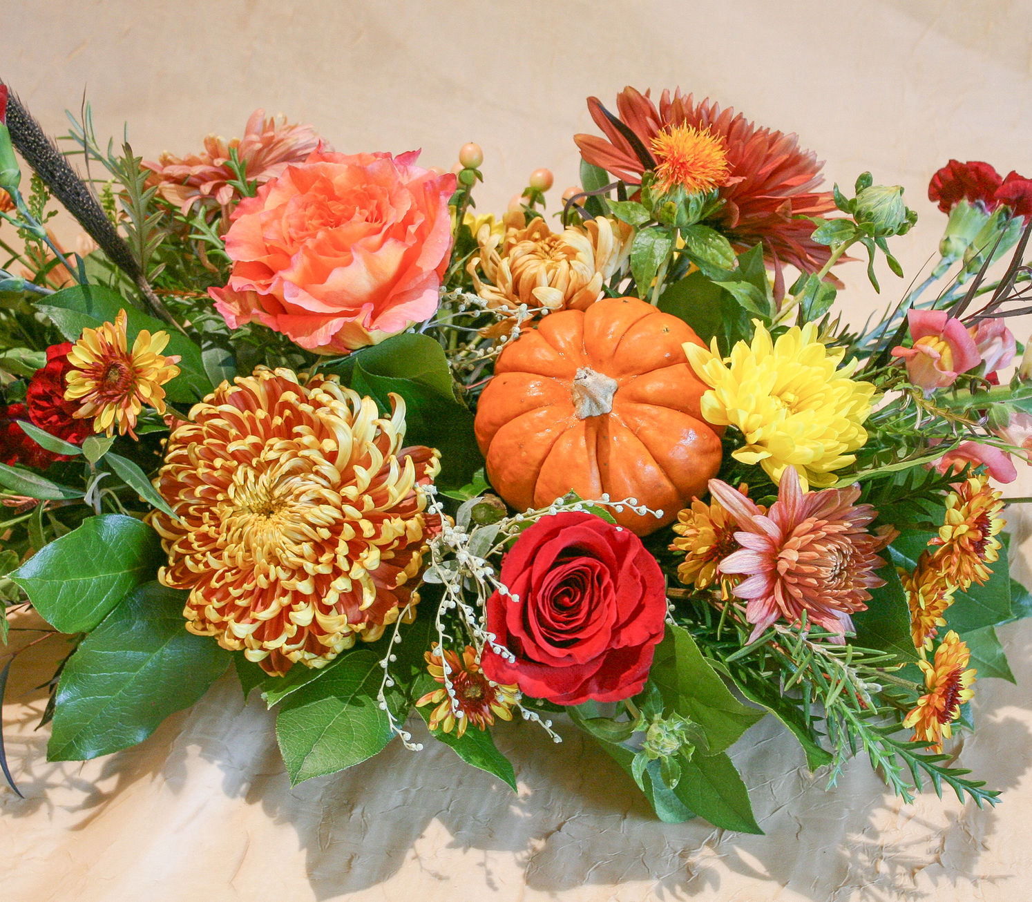 This festive Thanksgiving centerpiece features a stunning arrangement of vibrant blooms like mums, roses, snaps, and carnatio