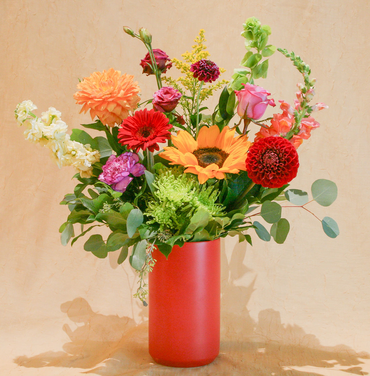 a fresh summer floral arrangement featuring a vibrant mix of warm red, orange, yellow, and purple blooms.