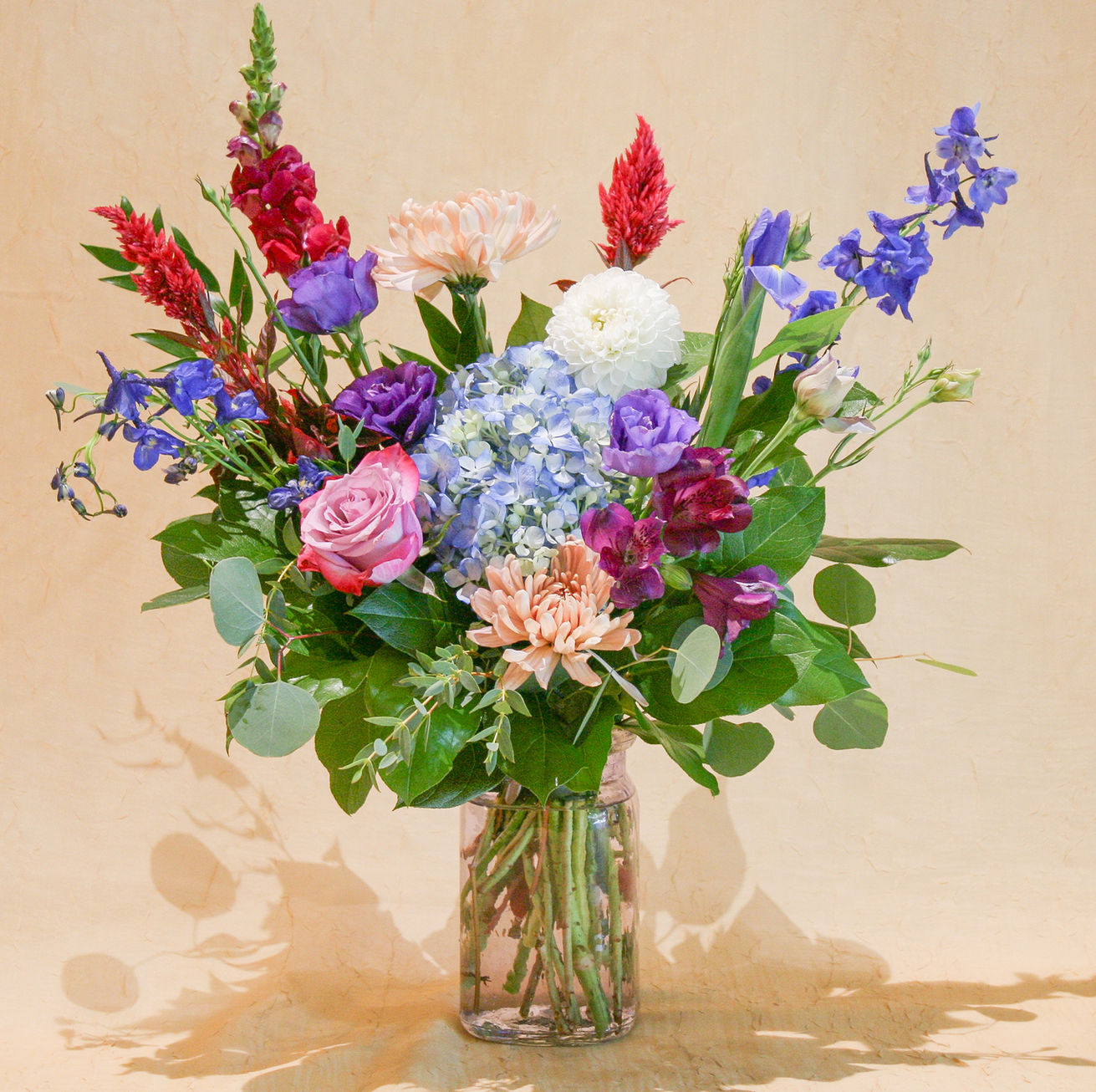a fresh summer floral arrangement of purple, blue, burgundy, and white blooms including dahlias in a purple vase