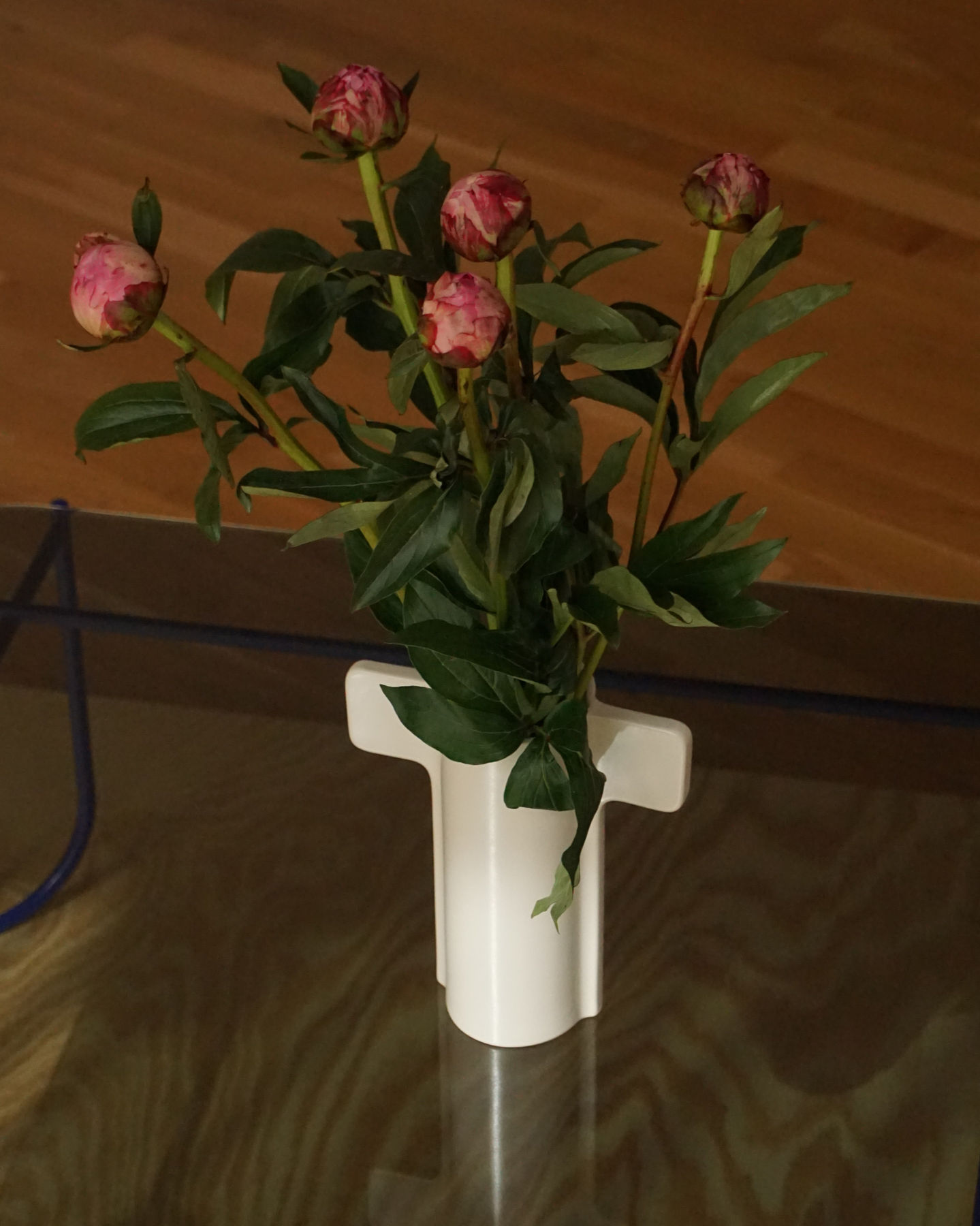 Pelarönn vase by designer Gustav Carlberg—a sculptural beige vase with distinctive handles, holding a bouquet of orange tulips. Placed on a wooden table near sheer curtains, the soft lighting enhances the elegant and natural aesthetic. elegant 