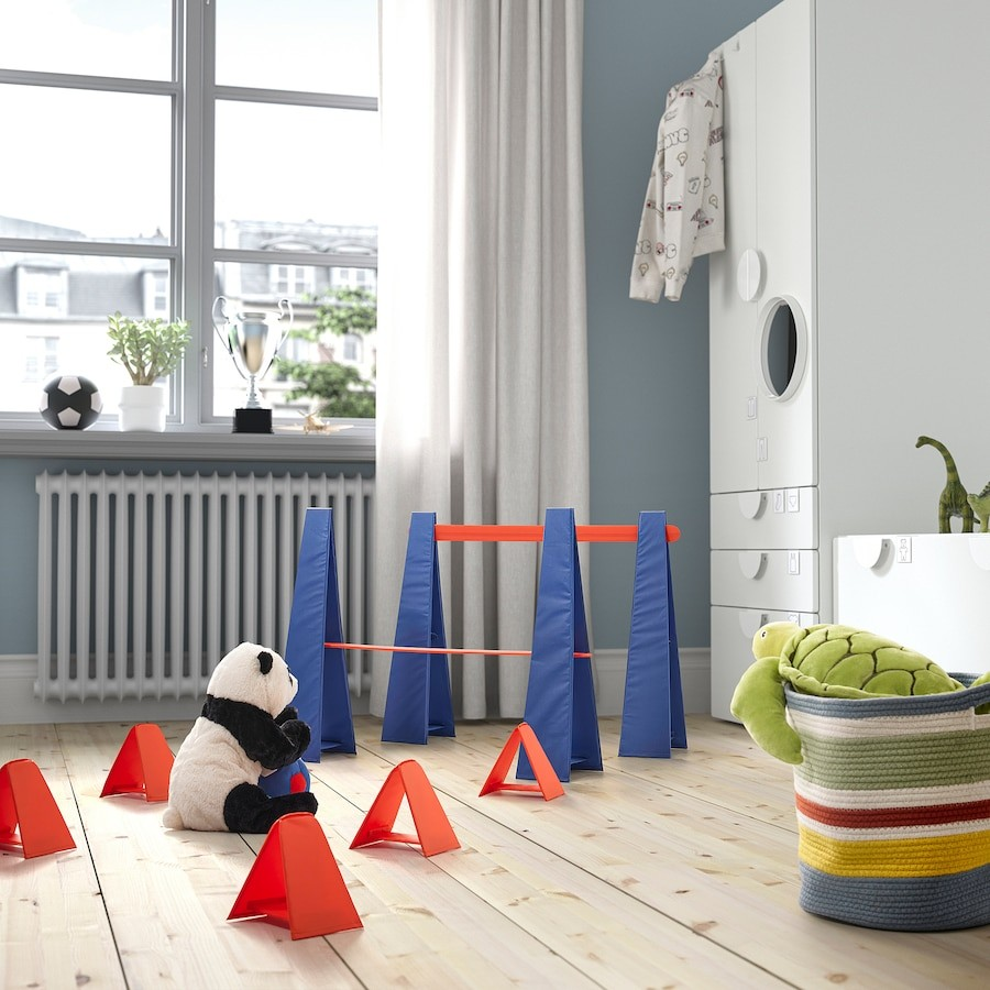 Skrattmås playroom setup—featuring red triangular cones and a blue-and-red obstacle structure for active play. A stuffed panda sits in the center, surrounded by playful elements. A striped basket with a green stuffed toy adds to the lively, engaging environment designed by Gustav.
