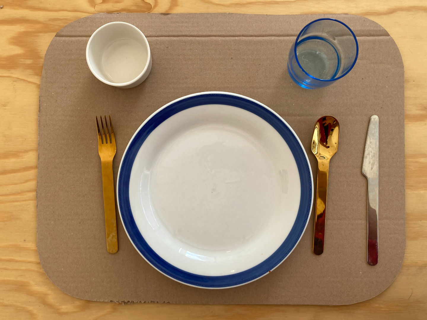 Mockup of Olseröd—exploring surface layout possibilities. A Scandinavian-inspired table setting with a white plate, gold utensils, and a blue glass, balancing aesthetics and functionality for modern interiors.