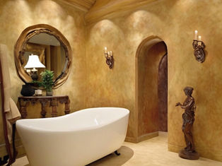 Elegant beige bathroom with a white freestanding tub, ornate mirror and sconces, bronze statue, and warm ambient lighting