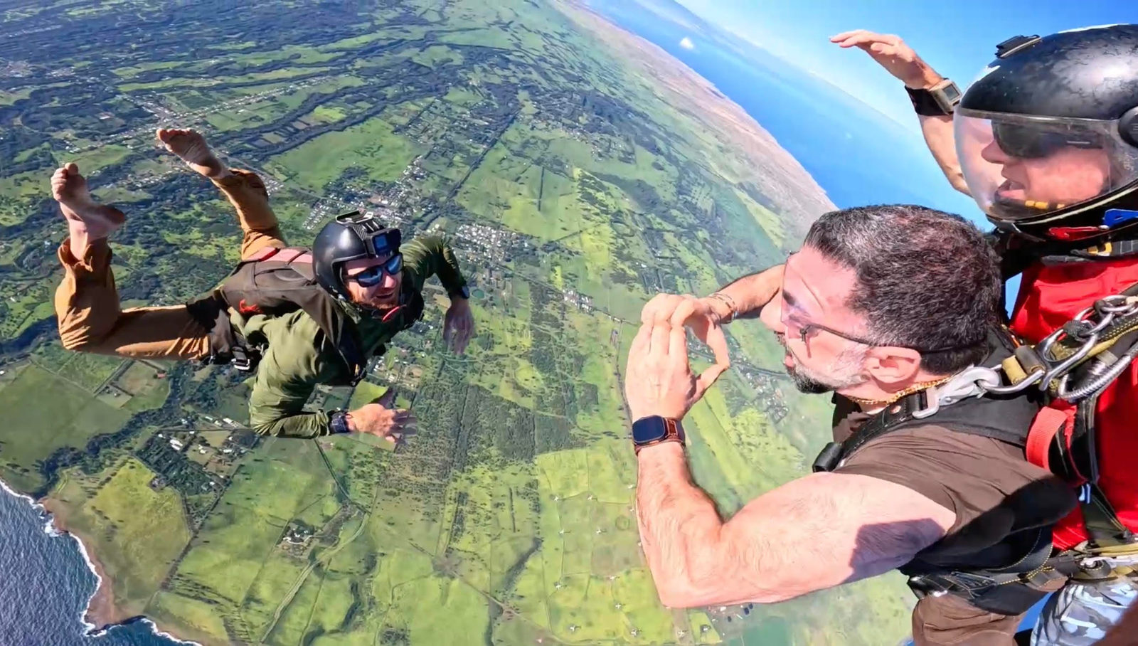 Tandem pair making a heart with their hands in freefall over the Big Island