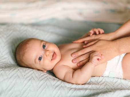 6 month baby laying on a bed in a diaper