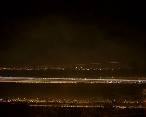 צילום פנורמי לילי של אורות עירוניים על רקע כהה, יוצר רצועת אור אופקית.