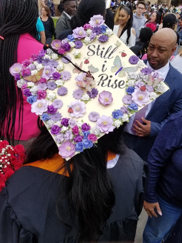 Jayla showing off her graduation cap adorned with "Still i rise" with a gold base and purpled flowers and butterflies