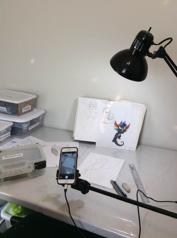 Bright artist studio with a desk lamp, art supplies, sketchbook, and phone. Set up for online teaching