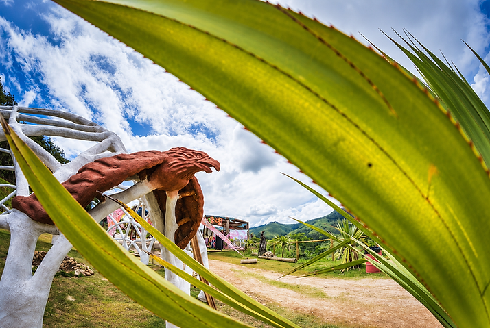Estrutura de arcos de barro brancos do Sistema Cobra com escultura da Harpia Sagrada integrada, enquadrada por vegetação tropical nativa e montanhas ao fundo na Aldeia Outro Mundo — bioconstrução por César Augusto Arquiteto Ecológico