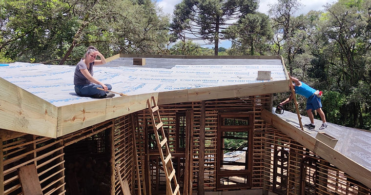 Instalação de manta anticondesação sobre estrutura de madeira roliça do telhado da Casa Nave Terra, em canteiro de bioconstrução.