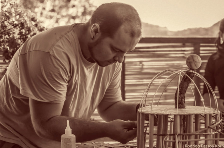 César Augusto, o arquiteto ecológico, concentrado na confecção manual de uma maquete de uma casa ecológica com cúpula de bambu, momento criativo e técnico de um projeto.