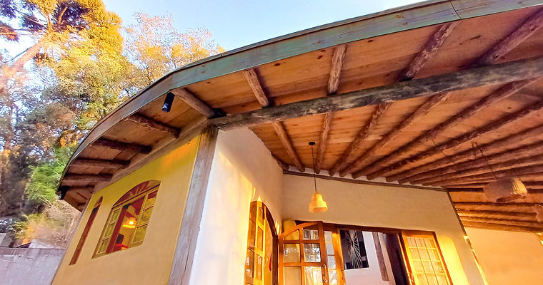 Varanda curva da Casa Nave Terra com vigamento radial de madeira roliça, teto trabalhado tábuas e esquadrias de madeira em paredes de pau-a-pique, em projeto de arquitetura ecológica de alto padrão.