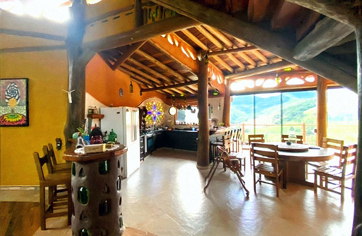 Interior da Casa da Árvore com pilares rústicos de troncos de madeira natural e ampla abertura de vidro, focando em projetos sustentáveis integrados à natureza.