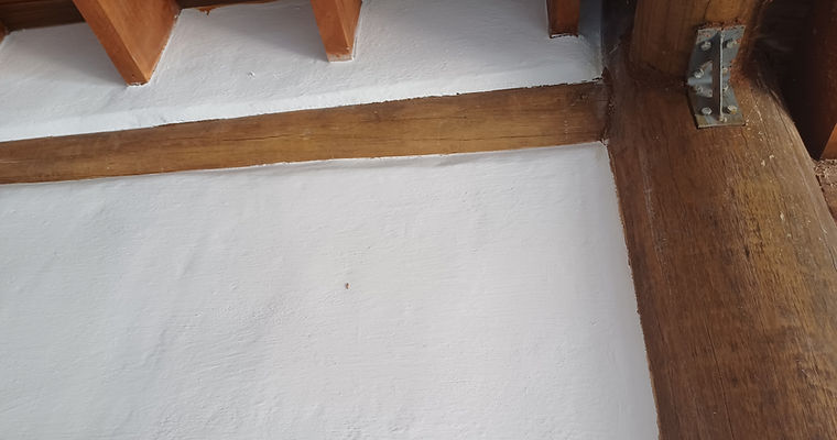 Detalhe de conexão de viga de madeira roliça com cantoneira metálica sobre parede de pau-a-pique com reboco natural e pintura de cal branco na Casa Essência da Vida, em conceito de arquitetura sustentável.