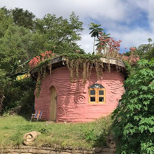Chalé ecológico para casais semienterrado na encosta do terreno com paredes de hiperadobe, teto verde e design orgânico tipo casa Hobbit.