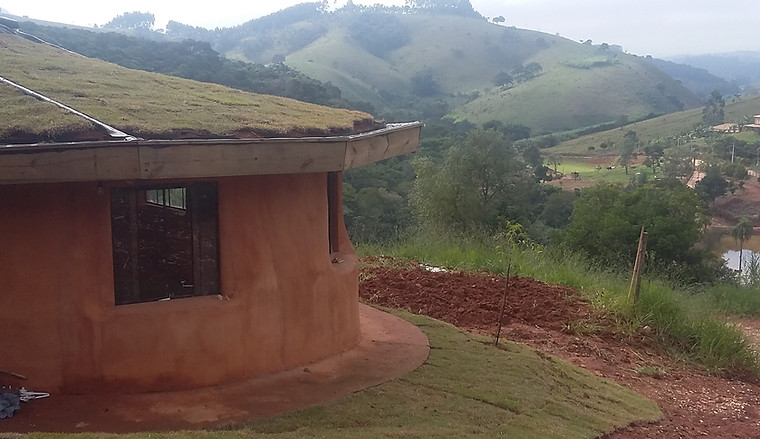 Vista lateral de chalé de terra com cobertura vegetal integrado à paisagem de montanhas e vale verdejante — arquitetura ecológica por César Augusto Arquiteto Ecológico
