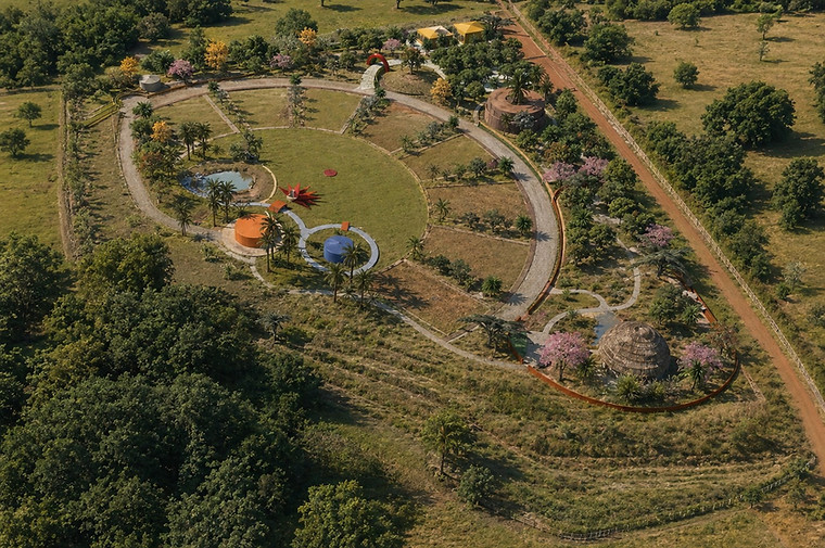 Maquete eletrônica 3D em vista aérea diurna de ecovila mostrando o traçado viário circular e praça central integrada à mata. Planejamento permacultural e de projetos sustentáveis por César Augusto Arquiteto.