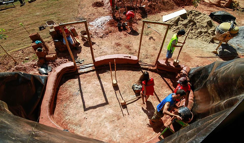 Aprendizes em curso prático de bioconstrução erguendo e compactando paredes curvas de hiperadobe para bloco de sanitários ecológicos — condução técnica por César Augusto Arquiteto Ecológico