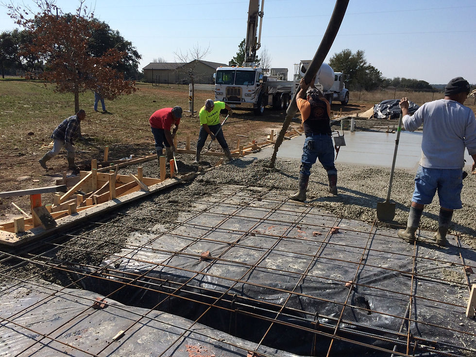 Construction crew pouring and leveling a concrete slab for a home addition project in Kyle, Texas, with rebar reinforcement, wood framing forms, and a concrete pump truck on-site.