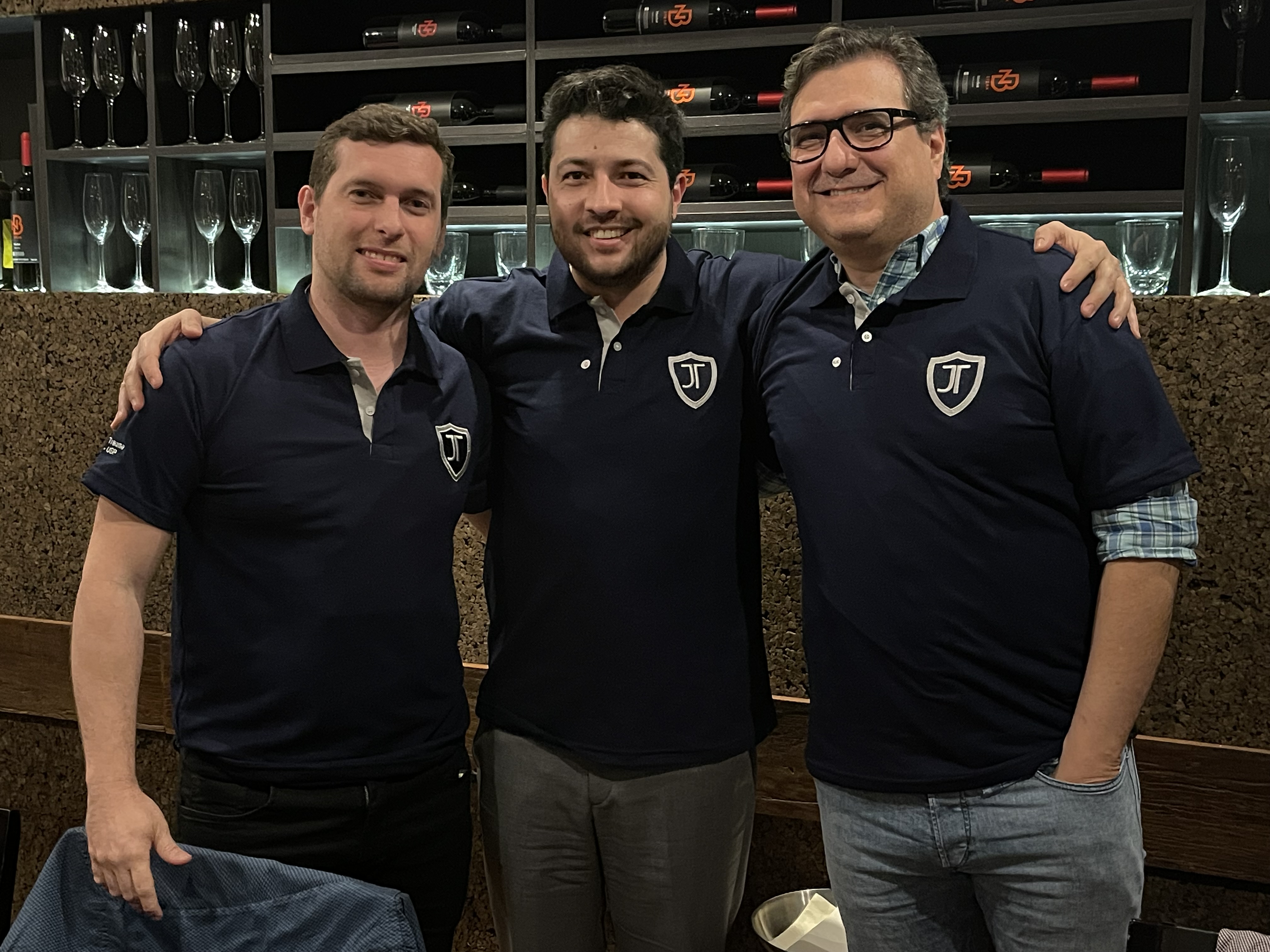 Três homens em camisas polo escuras com logo