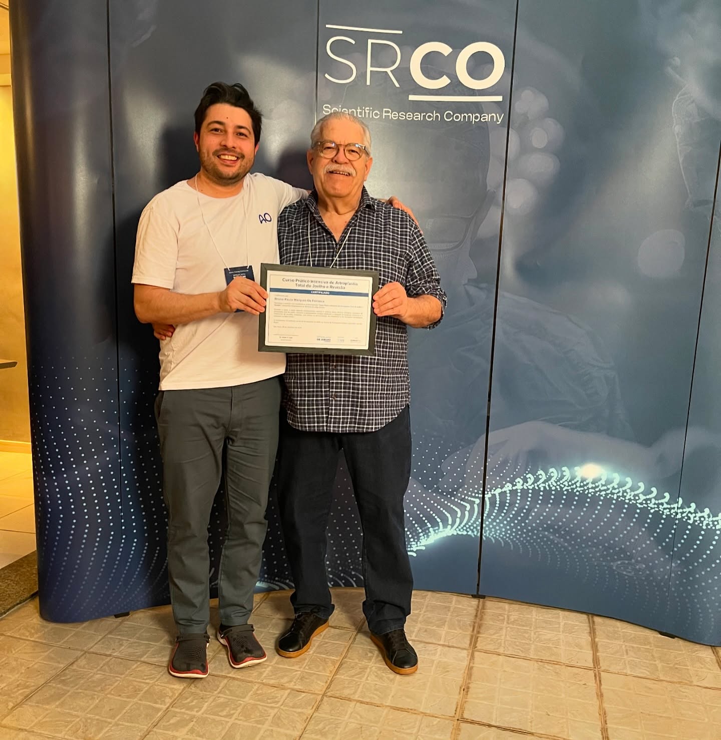 Dois homens sorrindo com certificado e painel SRCO