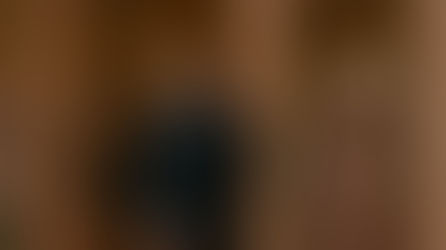 Security guard in a suit stands at a boutique entrance next to a mannequin in a peach dress. Interior shows soft lighting and hanging clothes.