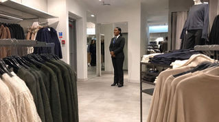 Security officer standing discreetly between clothing rails in a store.- Illustrative Image