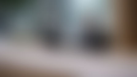 Smiling receptionist in a suit at a marble desk, with a computer and flowers, in a modern office lobby with large windows and plants.