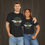 Thumbnail: Couple wearing our Black classic car t-shirt featuring a green background with a red wings circle design.
