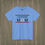 Thumbnail: Columbia blue Lacrosse Mom T-shirt with bold lettering and crossed lacrosse sticks featuring a USA flag design