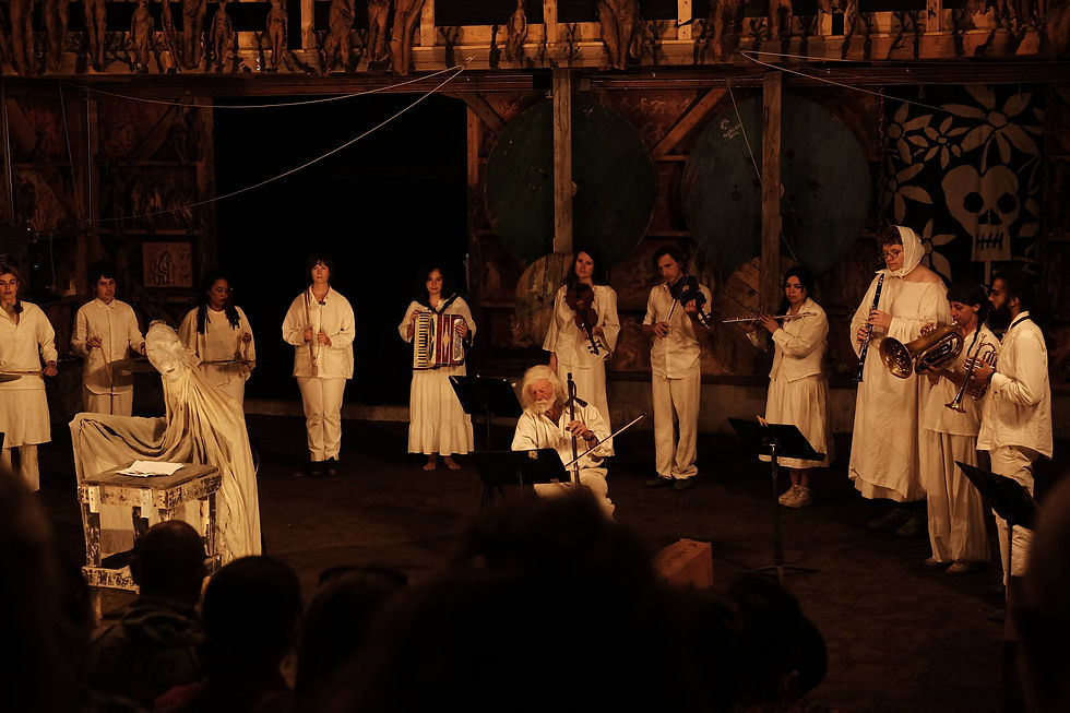 Musicians in white perform on stage with various instruments. A skeletal motif decorates the background. Mood is solemn and theatrical.
