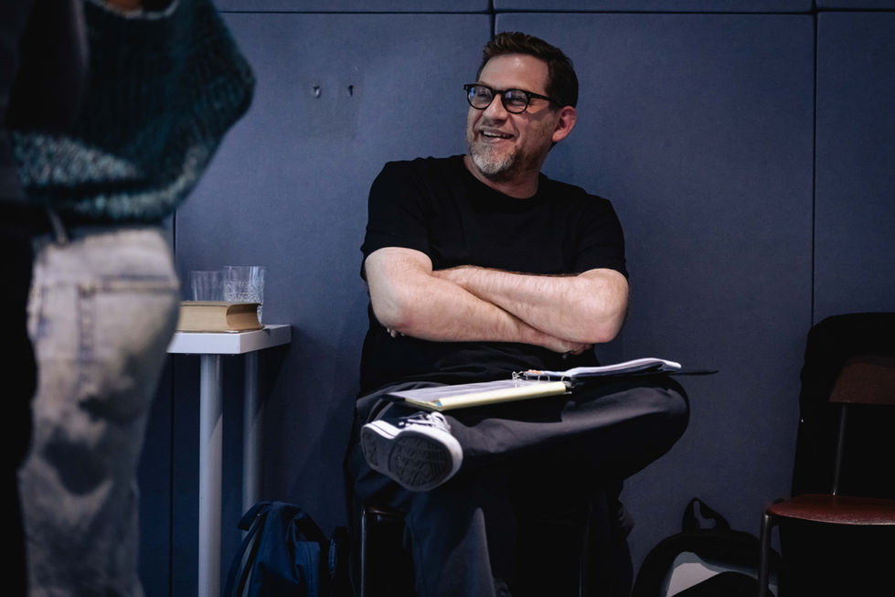 Man with beard in black T-shirt sitting down with notes on his lap