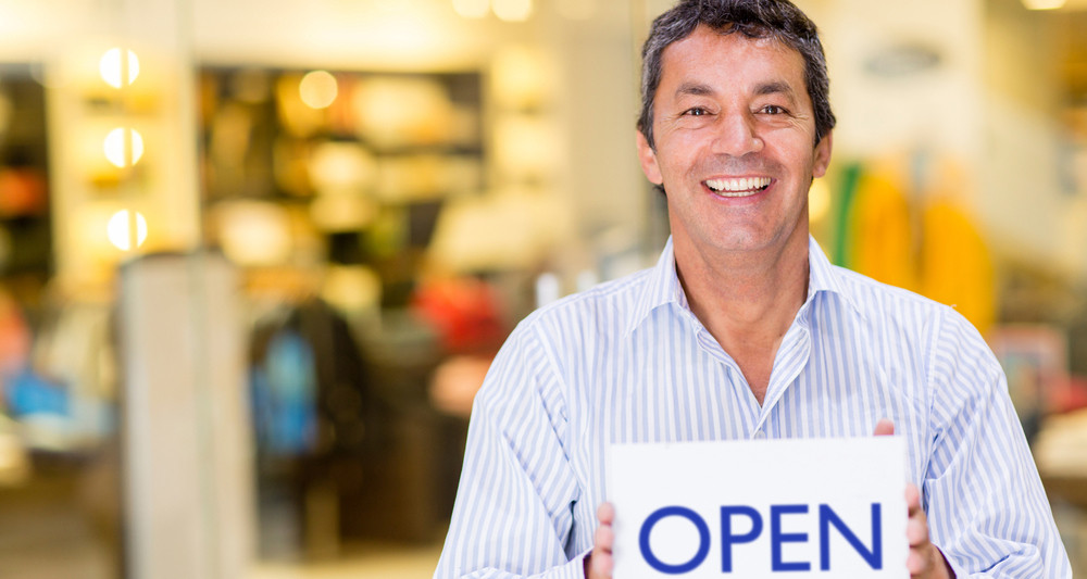 Male business owner holding an open sign and smiling