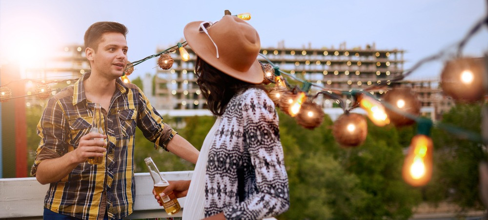 Multi-ethnic millenial couple flirting while having a drink on rooftop terrasse at sunset