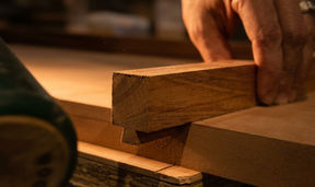Macro shot of a master artisan's hand fitting a precision timber joint in a workshop, emphasizing architectural joinery and natural wood grain.