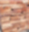 Stack of raw, solid wood planks in a shipyard setting, showcasing natural grain patterns, warm honey and reddish-brown tones, and varying textures.
